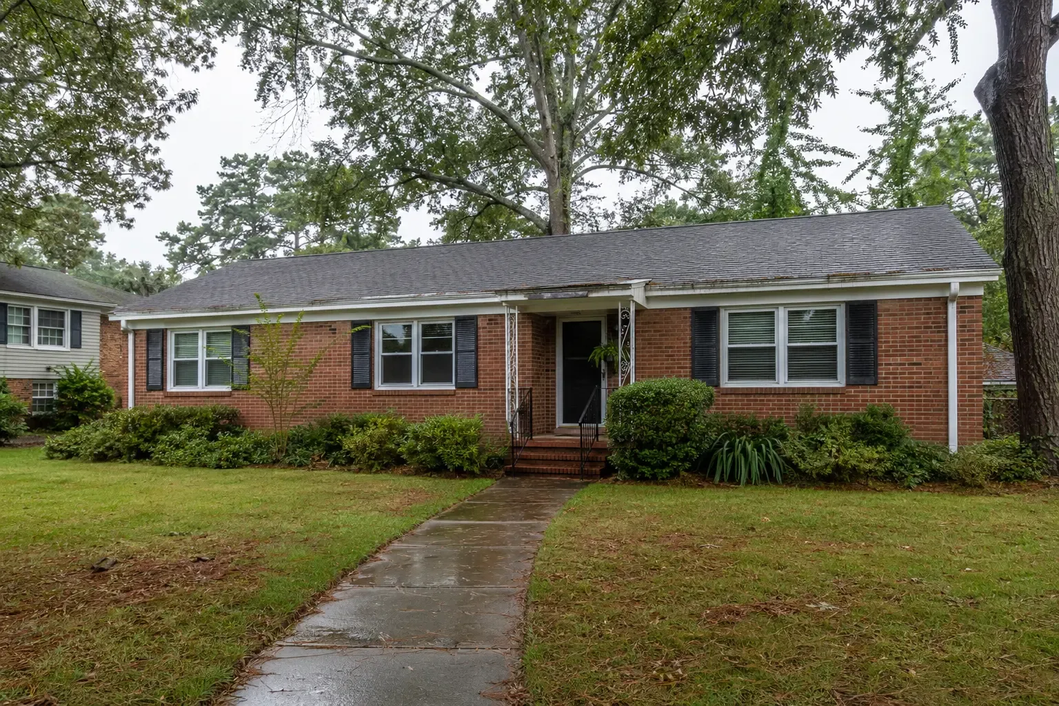 A brick home on a tree-lined street after rain