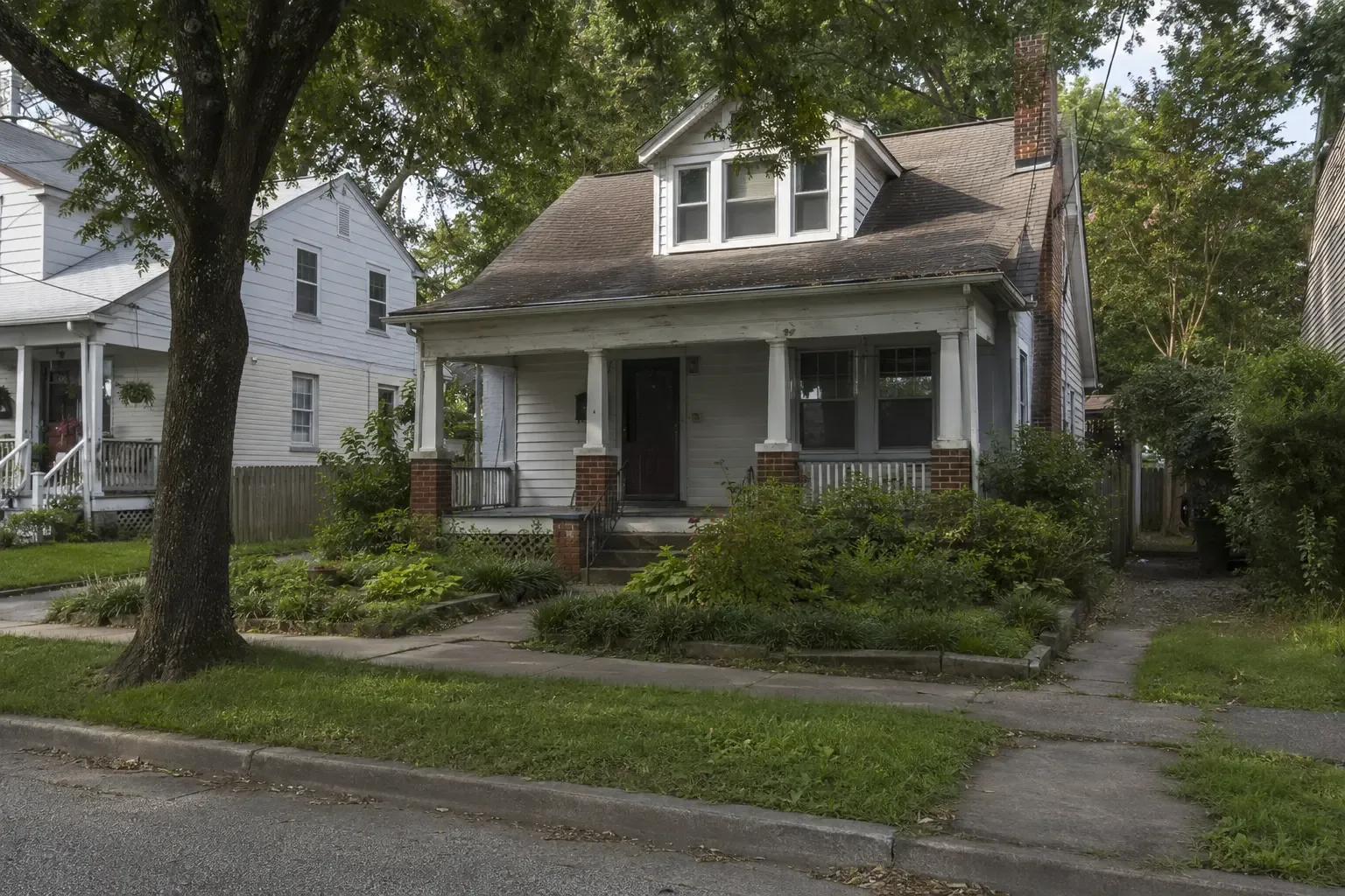 An older home with a shaded porch and mature trees