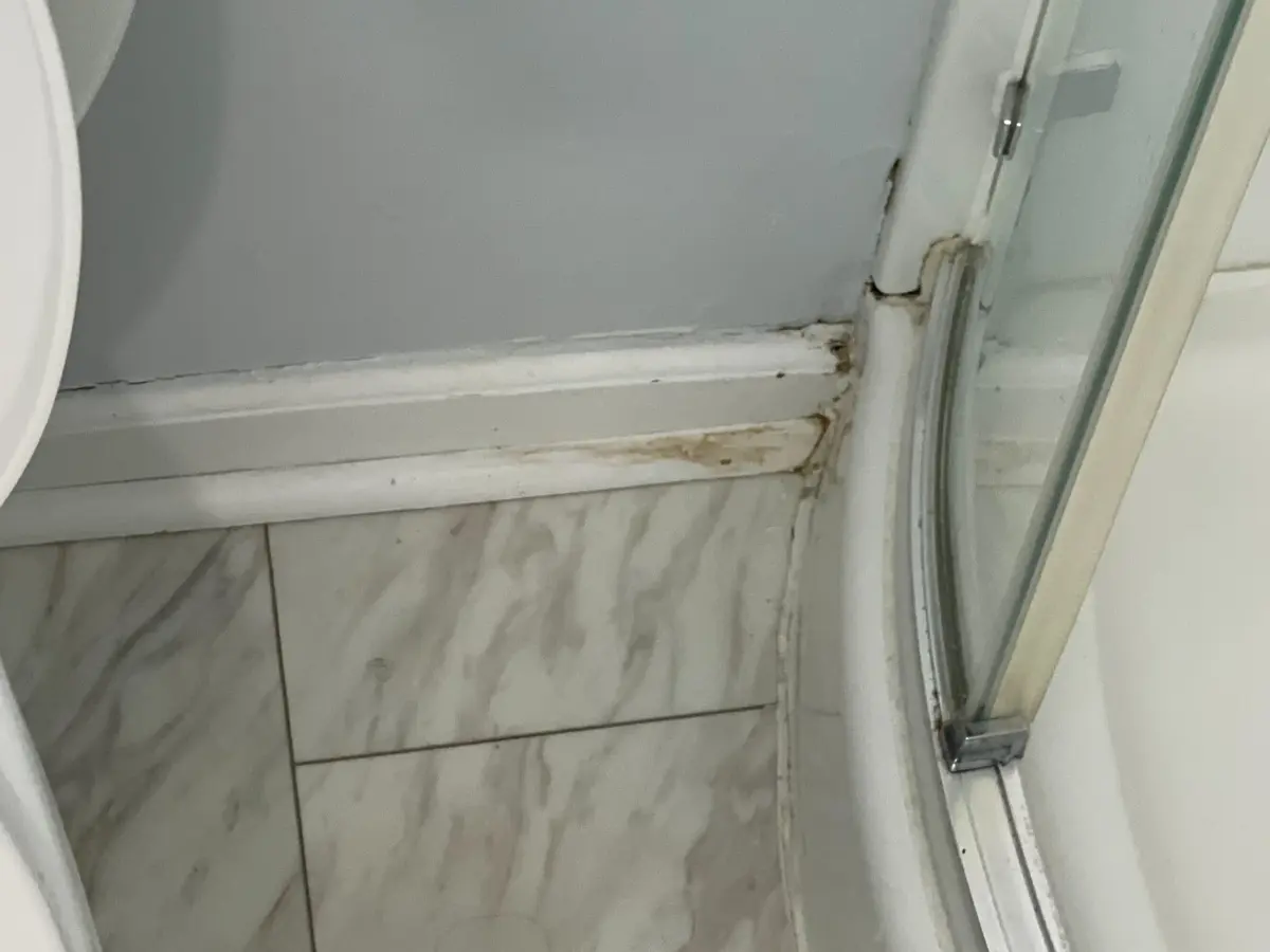 Water damage and deteriorated caulk beside a shower enclosure before repair